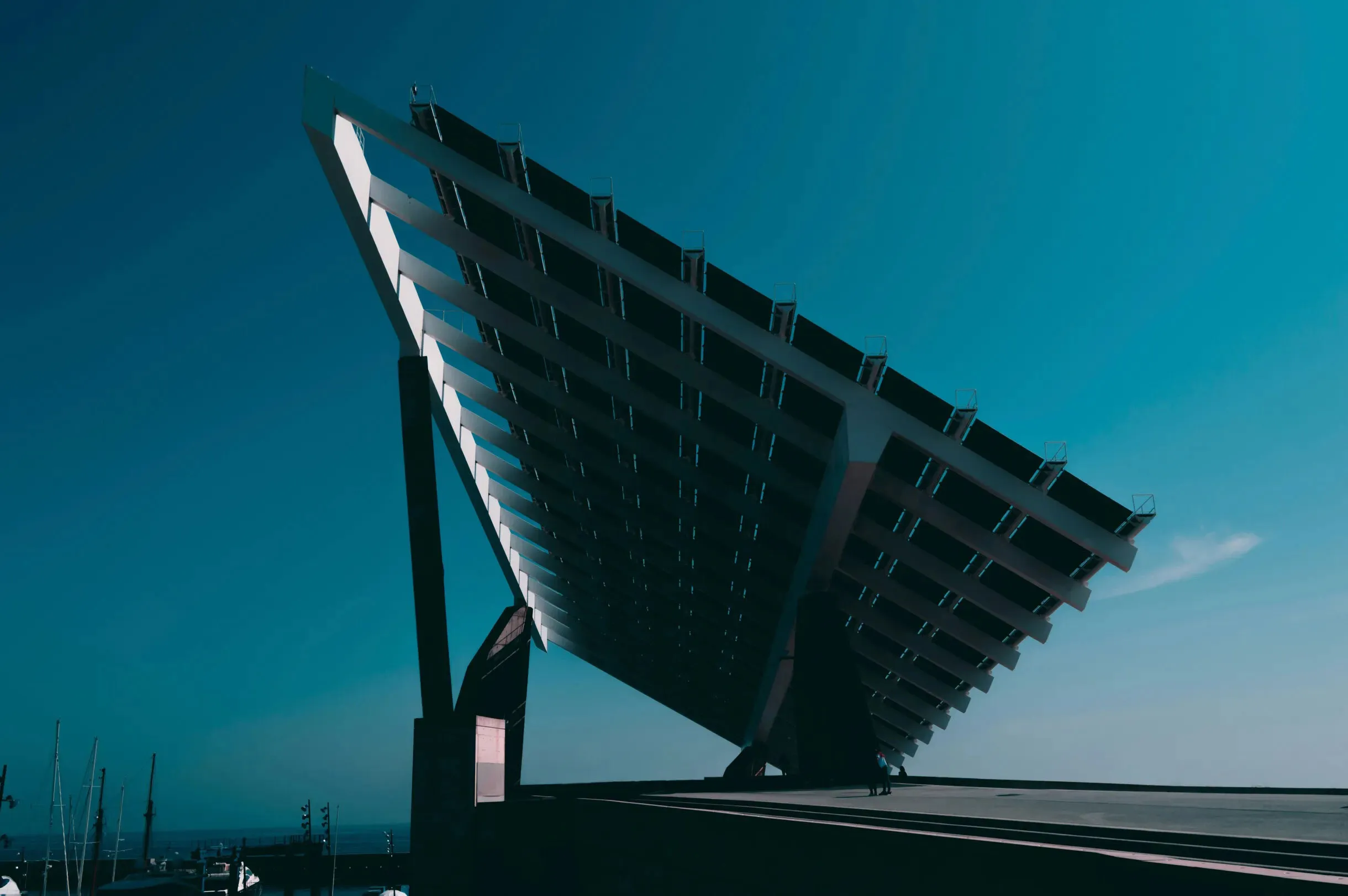 Large angled solar panel structure under a clear blue sky near a marina.