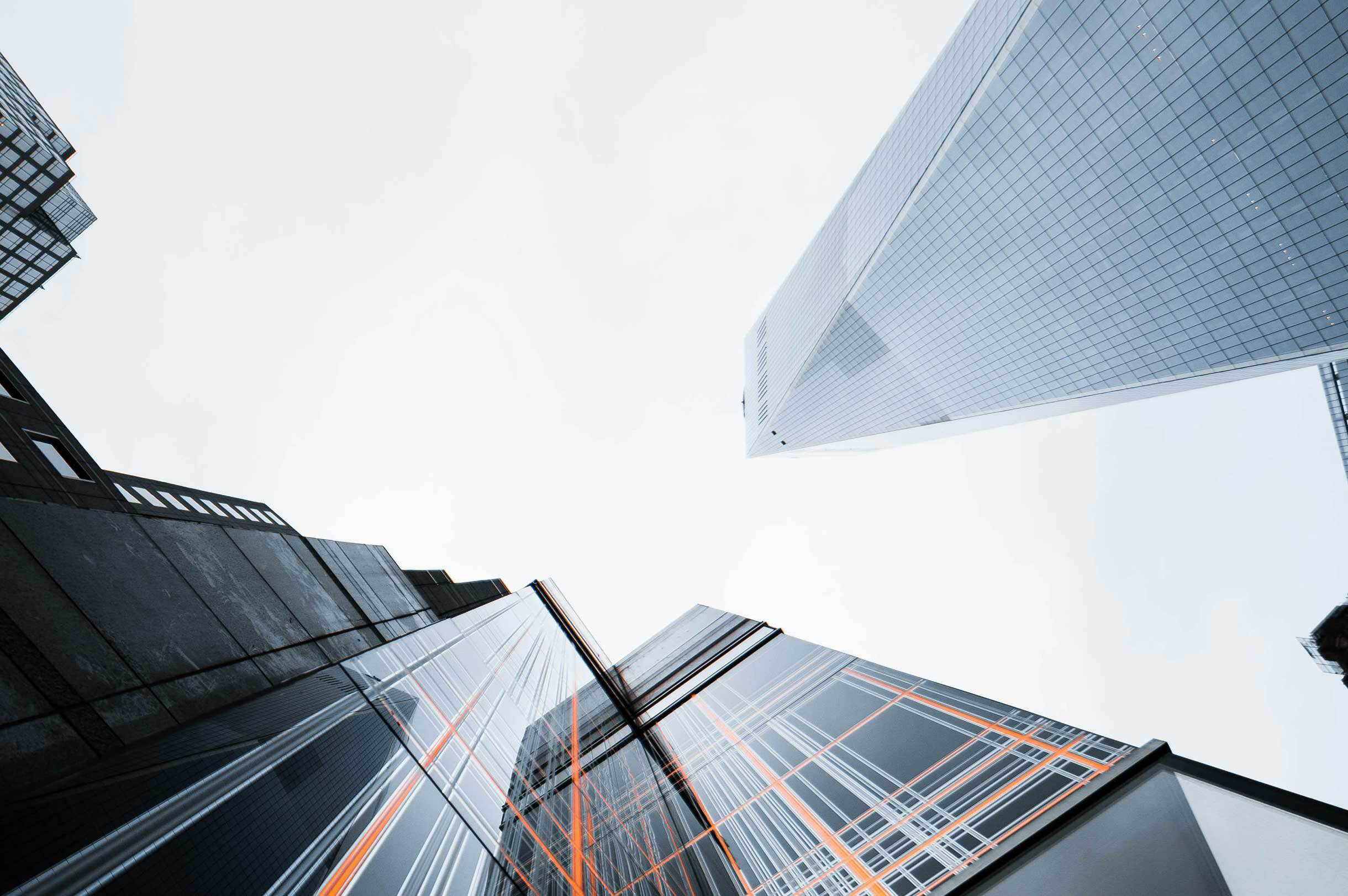 Upward view of modern skyscrapers with glass facades reflecting the sky and nearby buildings.