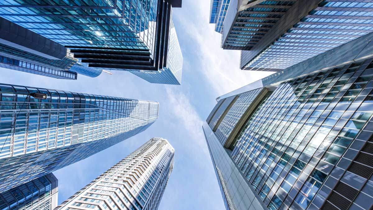 Low-angle view of tall modern skyscrapers with glass facades under a cloudy sky.